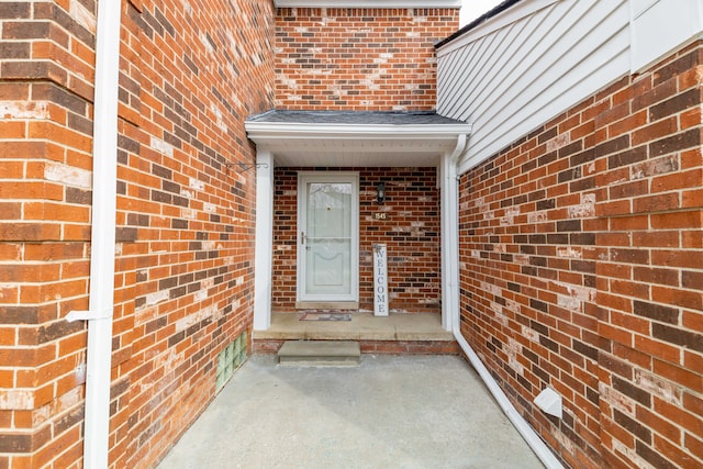 doorway to property featuring brick siding and a shingled roof