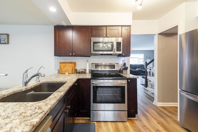 kitchen featuring light stone counters, light wood-style flooring, a sink, dark brown cabinets, and appliances with stainless steel finishes