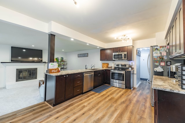 kitchen with light wood-style flooring, a sink, appliances with stainless steel finishes, a fireplace, and dark brown cabinets