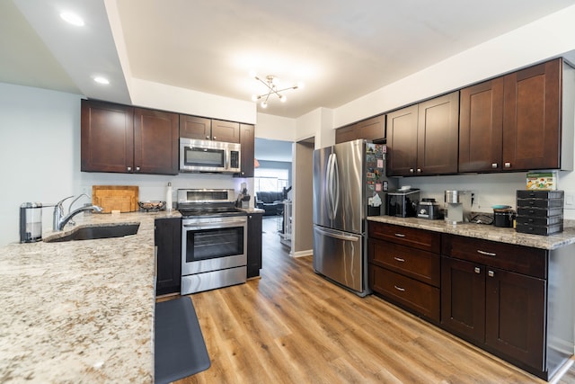 kitchen featuring light stone counters, a sink, appliances with stainless steel finishes, light wood finished floors, and dark brown cabinets