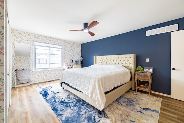 bedroom featuring visible vents, wallpapered walls, ceiling fan, baseboards, and wood finished floors