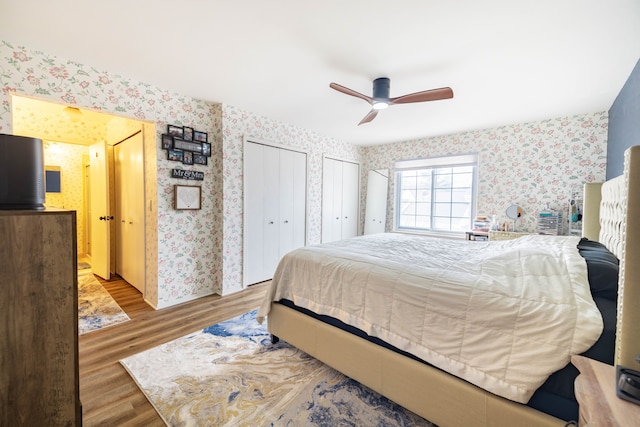 bedroom with wallpapered walls, wood finished floors, multiple closets, and ceiling fan