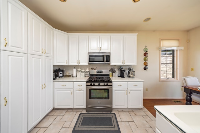 kitchen with stainless steel appliances, tasteful backsplash, light countertops, and white cabinetry