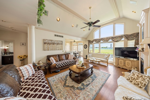 living area with decorative columns, visible vents, hardwood / wood-style flooring, ceiling fan, and high vaulted ceiling