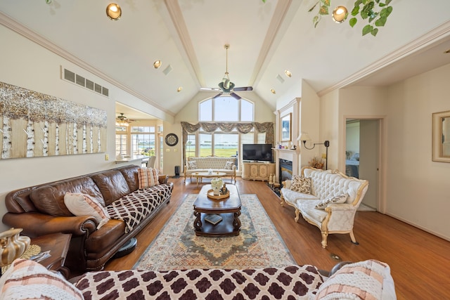 living room featuring wood finished floors, visible vents, a ceiling fan, beamed ceiling, and a glass covered fireplace