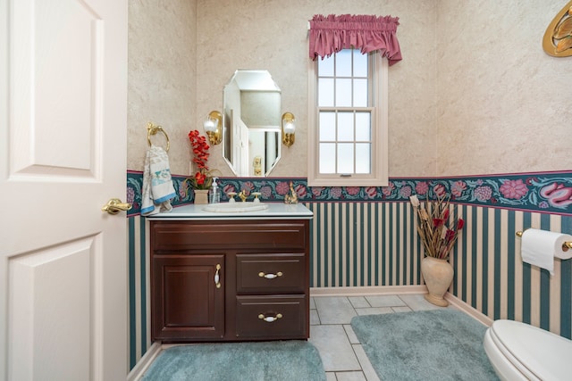 half bath featuring wallpapered walls, baseboards, toilet, tile patterned floors, and vanity