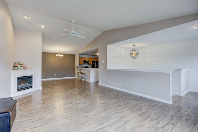 unfurnished living room with light wood-type flooring, lofted ceiling, a glass covered fireplace, and ceiling fan with notable chandelier