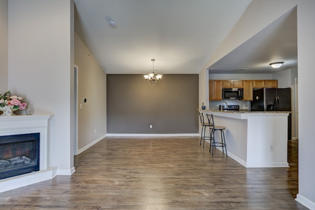 kitchen with a breakfast bar area, a fireplace, wood finished floors, black fridge with ice dispenser, and stainless steel microwave