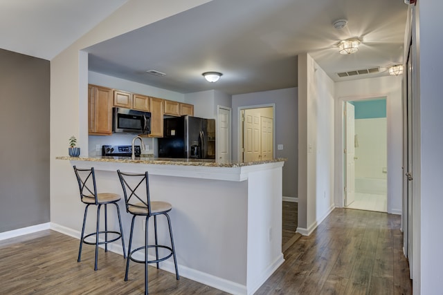 kitchen featuring dark wood-style floors, black fridge, a kitchen bar, and visible vents