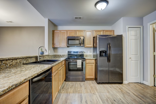 kitchen with stainless steel appliances, a sink, visible vents, light stone countertops, and light wood finished floors