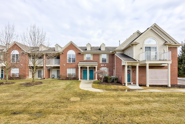 view of front facade with a balcony, a front lawn, and brick siding