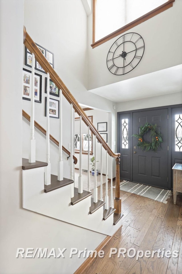 entryway featuring a towering ceiling, wood-type flooring, and stairs