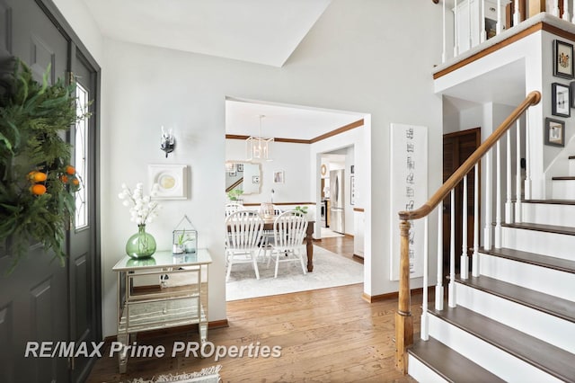 foyer entrance featuring baseboards, stairway, wood finished floors, a healthy amount of sunlight, and a notable chandelier