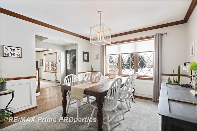 dining area featuring light wood finished floors, ornamental molding, a wainscoted wall, and an inviting chandelier