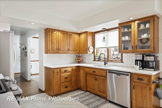 kitchen featuring brown cabinets, decorative backsplash, freestanding refrigerator, a sink, and dishwasher