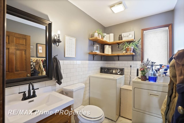 bathroom with tile walls, toilet, wainscoting, vanity, and independent washer and dryer