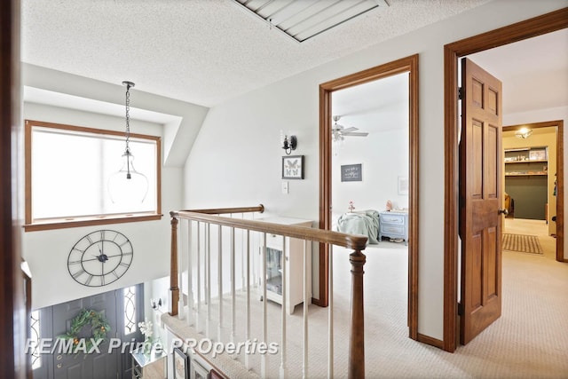 hallway featuring carpet floors, a textured ceiling, and an upstairs landing