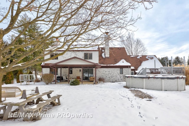 snow covered back of property with stone siding, a covered pool, and a chimney