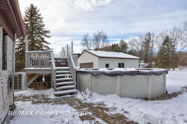 view of snow covered exterior with a garage, a covered pool, stairway, and a wooden deck