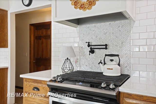 kitchen with brown cabinetry, custom range hood, stainless steel gas range oven, and decorative backsplash