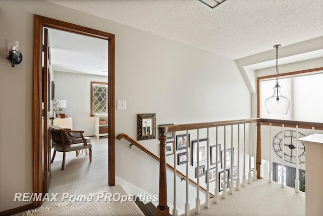 hall with carpet floors, baseboards, a textured ceiling, and an upstairs landing