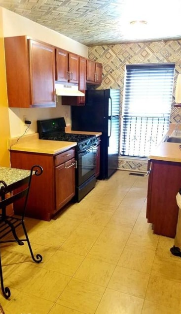 kitchen featuring under cabinet range hood, freestanding refrigerator, light countertops, and gas stove