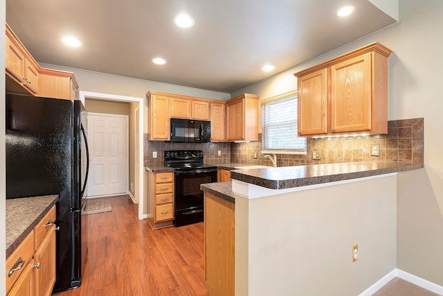 kitchen with black appliances, wood finished floors, a peninsula, and tasteful backsplash