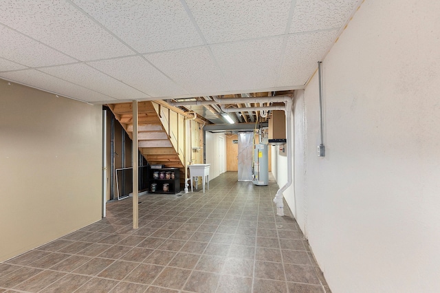 finished basement with a drop ceiling, water heater, and tile patterned flooring