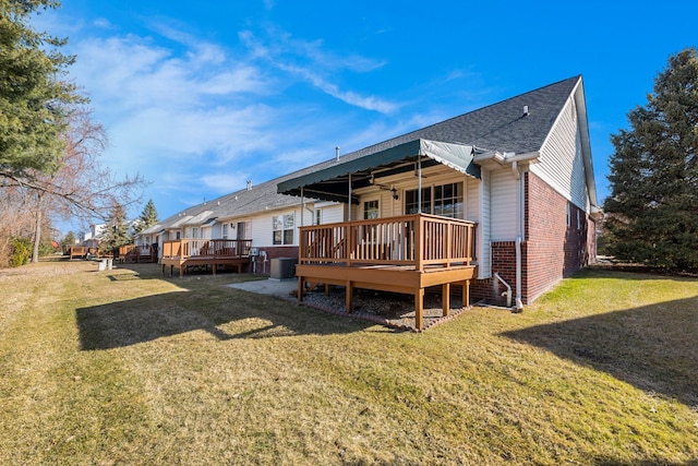 back of house with a shingled roof, a lawn, brick siding, and a wooden deck