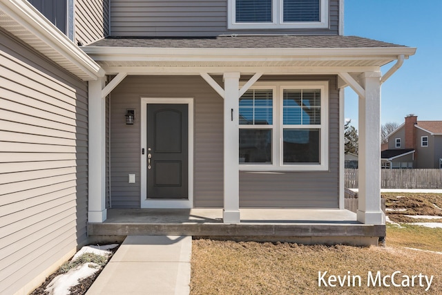 doorway to property with covered porch, roof with shingles, and fence