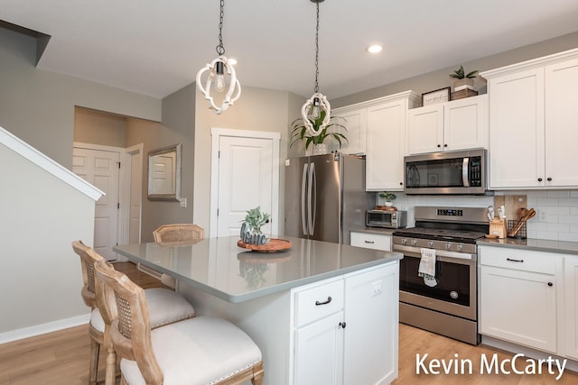 kitchen featuring light wood-style floors, white cabinets, appliances with stainless steel finishes, backsplash, and a center island