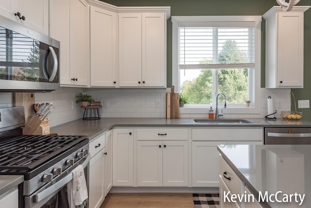 kitchen featuring appliances with stainless steel finishes, white cabinets, a sink, and decorative backsplash