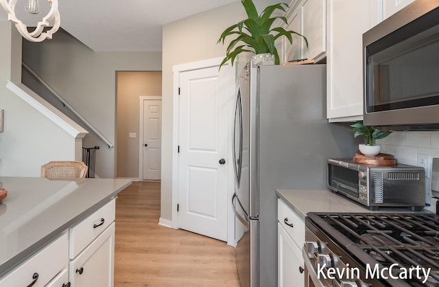 kitchen featuring light wood-type flooring, stainless steel microwave, decorative backsplash, and white cabinetry