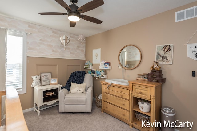 living area with light carpet, visible vents, a ceiling fan, and wainscoting