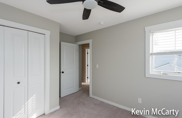 unfurnished bedroom with a ceiling fan, a closet, light carpet, and baseboards