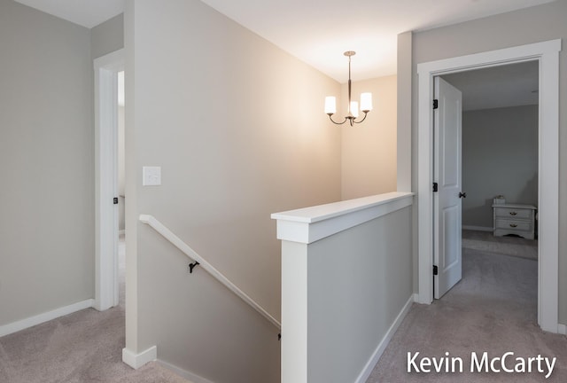 hallway with an inviting chandelier, carpet, baseboards, and an upstairs landing