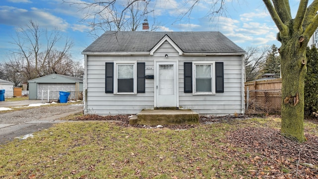 bungalow with a garage, a shingled roof, a chimney, an outbuilding, and fence