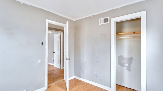 unfurnished bedroom with a closet, visible vents, baseboards, and wood finished floors