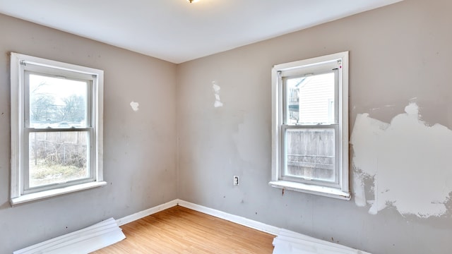 empty room featuring light wood-type flooring, plenty of natural light, and baseboards