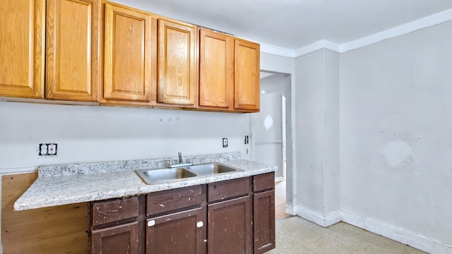 kitchen with crown molding, baseboards, light countertops, and a sink