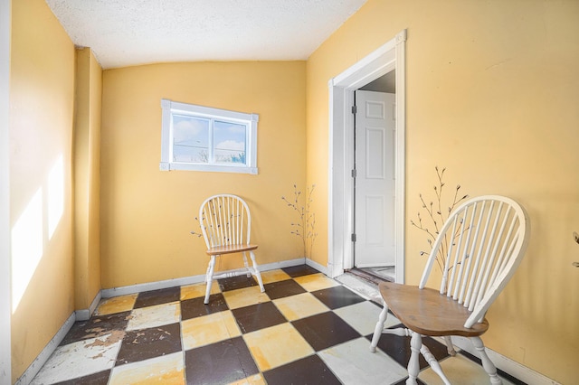 interior space featuring baseboards, a textured ceiling, vaulted ceiling, and tile patterned floors