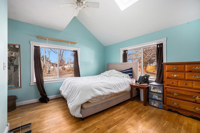 bedroom featuring light wood-type flooring, lofted ceiling with skylight, ceiling fan, and baseboards