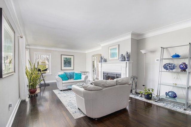 living room featuring a warm lit fireplace, arched walkways, dark wood-style flooring, baseboards, and ornamental molding