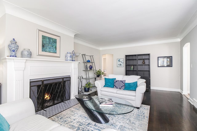 living area with arched walkways, crown molding, dark wood finished floors, a lit fireplace, and baseboards