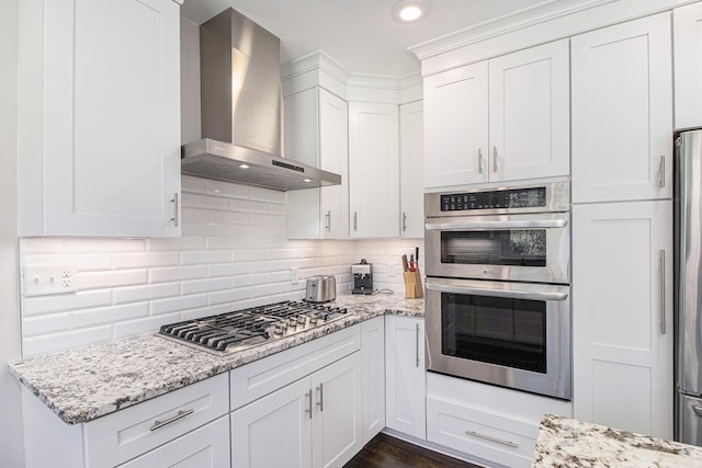 kitchen with decorative backsplash, appliances with stainless steel finishes, white cabinetry, light stone countertops, and wall chimney exhaust hood