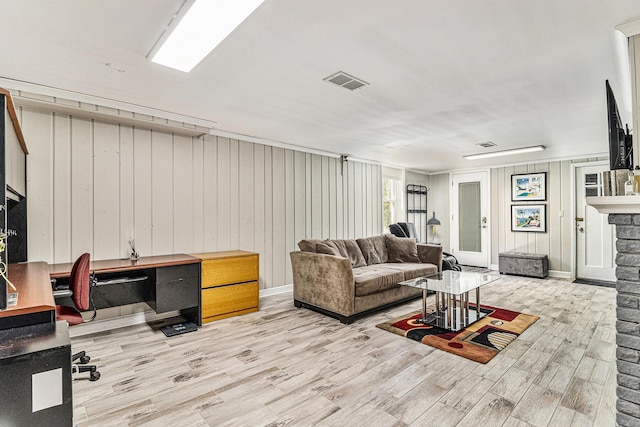 living area with light wood-type flooring, visible vents, and a stone fireplace