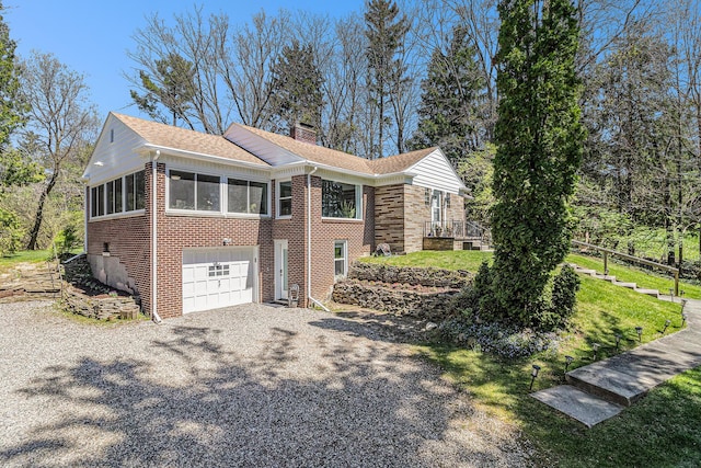 view of property exterior with an attached garage, brick siding, a chimney, and gravel driveway