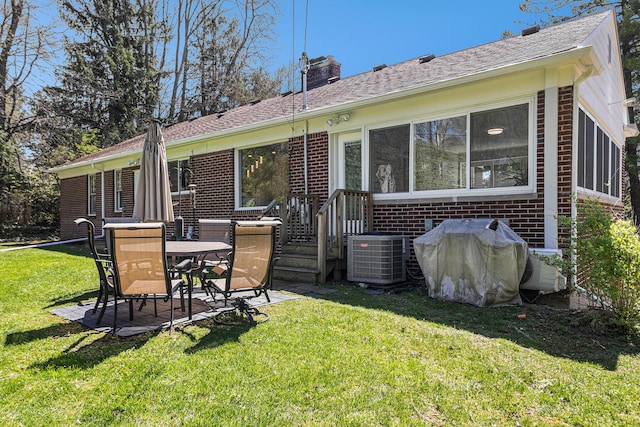 rear view of house featuring brick siding, roof with shingles, a lawn, a chimney, and a patio area