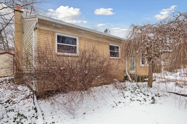 view of snow covered exterior with brick siding and a chimney