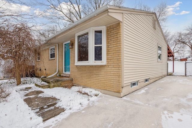 view of snow covered exterior featuring fence and brick siding